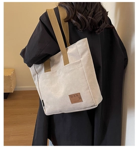 Detail view of large canvas tote bag featuring premium leather logo and wide shoulder straps