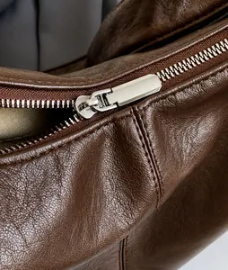 Macro detail of polished silver zipper and lychee texture on brown leather bag