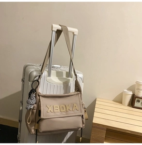 Detail of a khaki tote bag with XBOKA patch and a checkered bunny charm on a suitcase