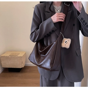 Detail of dark brown hobo crossbody bag with wide strap and plush monster charm