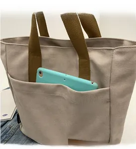 Detail of spacious front pocket on beige canvas tote bag with brown straps