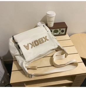 Close-up of cream messenger bag with XBOKA letter patch on a vintage wooden table