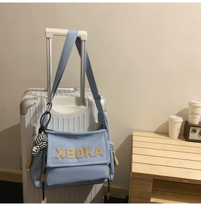 Detail of light blue crossbody tote bag with XBOKA patch and checkerboard charm hanging