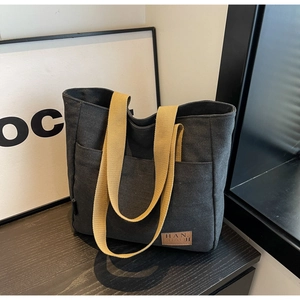 Detail of canvas tote bag showing brown leather logo patch and contrast ginger straps