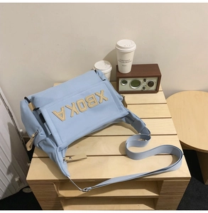 Detail of light blue tote bag showing XBOKA logo patch and adjustable woven strap