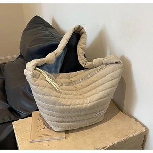 Détail d'un sac bandoulière matelassé beige en nylon avec sangle nouée sur pierre