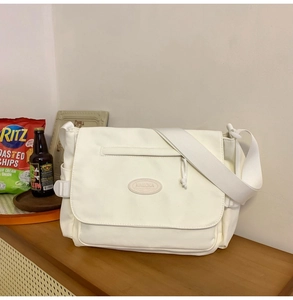 Detalle del bolso mensajero blanco de nailon con solapa y logo sobre una mesa de madera