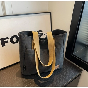 Detail of dark canvas tote bag featuring an external pocket and wide khaki shoulder strap