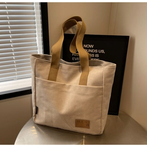 Close-up of the beige canvas tote bag showing the exterior pocket and brown leather patch