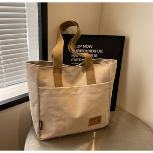 Detail of off-white canvas tote bag with brown handles and a leather brand label