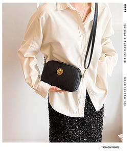 Sac bandoulière en cuir noir matelassé avec emblème doré et sangle fine sur le corps