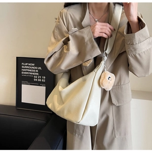 Macro detail of creamy beige dumpling bag with soft lychee leather texture and bear charm