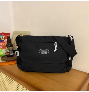 Detalle de bolso mensajero de nailon negro con correa ajustable y solapa con logotipo