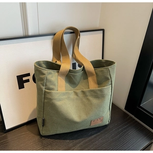 Detailed close-up of army green canvas tote bag featuring outer pocket and brand tag