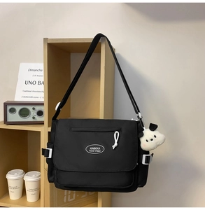 Detalle de un bolso tote utilitario de nailon negro con colgante de perro de peluche