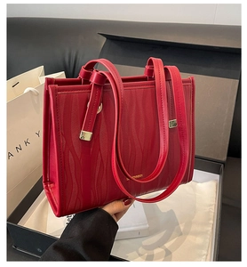 Detail of red embossed tote bag with gold hardware and brand logo in gift box