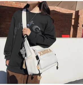 Detailed view of the white XBOKA messenger bag with wide shoulder strap and charm