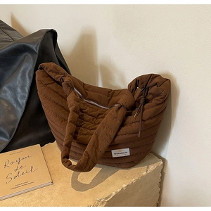 Détail de la texture matelassée du sac en nylon marron et étiquette sur socle en pierre