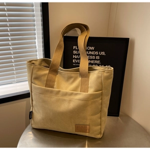 Detailed close-up of a beige canvas tote bag with front pocket and leather logo patch