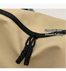 Detail view of the smooth black zipper and woven cord puller on khaki nylon bag