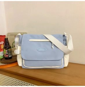 Detalle del bolso de mensajero azul y blanco con el logo ovalado de goma en la solapa