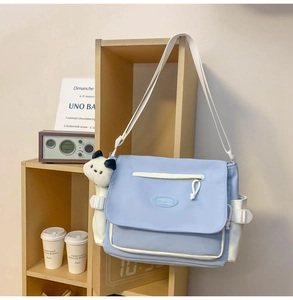 Detalle del bolso mensajero azul claro con bolsillo de contraste y colgante de peluche