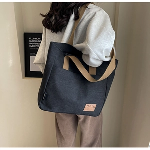 Detail of a large canvas tote bag with brown straps and leather logo for women