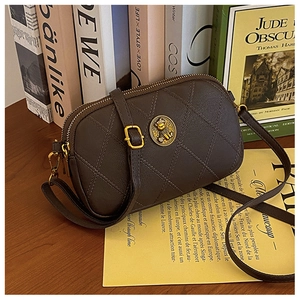 Détail du sac caméra matelassé marron foncé avec emblème d'ours doré et double fermeture