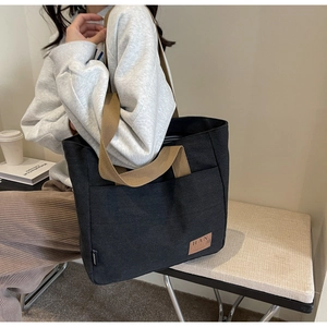 Close-up of black canvas tote bag with brown leather brand tag and woven handles
