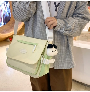 Detalle de bolso mensajero verde y beige con un lindo colgante de perro blanco de peluche