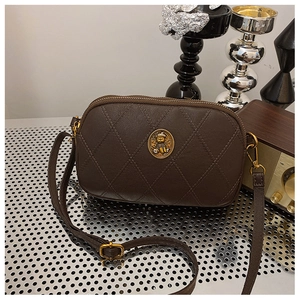 Détail d'un sac bandoulière matelassé marron foncé avec badge ours doré et fermeture éclair