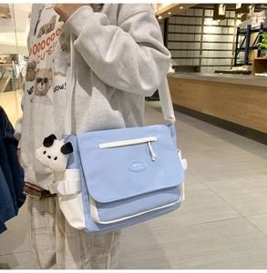 Detalle del bolso mensajero azul claro con correas blancas y colgante de panda de peluche