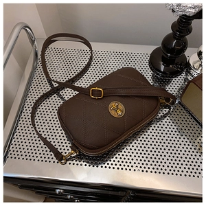 Détail du sac bandoulière matelassé marron foncé avec emblème doré sur étagère métal