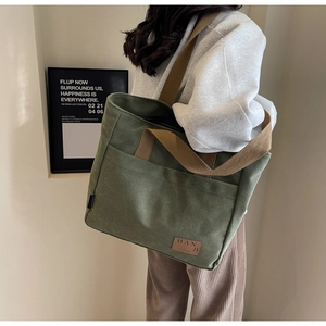 Detail view of large olive green canvas tote bag featuring side pocket and brand logo