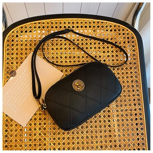 Détail du sac à bandoulière en cuir matelassé noir avec emblème doré sur du rotin