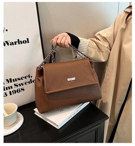 Detail of dark brown pleated tote bag featuring texture and metal chain accent