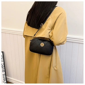 Détail du sac bandoulière noir matelassé avec emblème doré sur un trench-coat chic