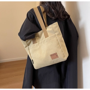 Detail of khaki canvas tote bag with brown straps worn over a black coat
