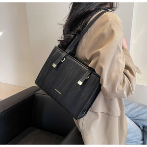 Side view of structured black leather handbag with gold accents and wave texture pattern