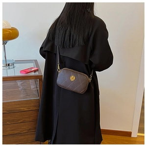 Détail du sac bandoulière matelassé marron foncé avec boucle dorée et trench-coat noir