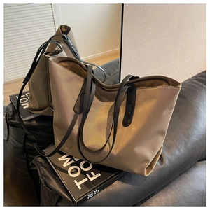 Détail du sac cabas en nylon doré champagne avec lanières en cuir noir sur surface réfléchissante