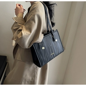 Detail of black wave-patterned tote bag with gold hardware worn with a trench coat