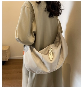 Detail of beige nylon half-moon bag featuring knot zipper pulls and brand tag