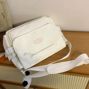 Bolso mensajero de nailon blanco crema con correa ancha y colgante de panda en mueble madera