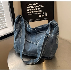 Dettaglio borsa tote in denim blu con cuciture bianche e bordi con frange
