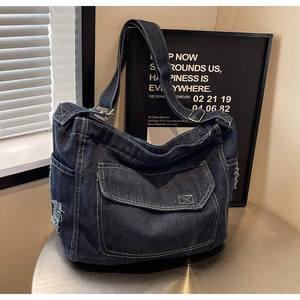 Dettaglio borsa a tracolla in denim blu scuro con cuciture bianche a contrasto e bordi logori