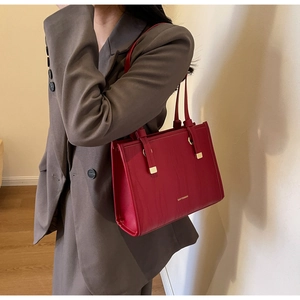 Detail of red ripple textured tote bag featuring gold hardware and logo on deep red surface