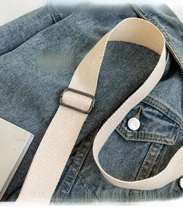 Detail of adjustable off-white nylon strap with dark grey metal buckle on denim