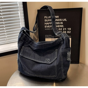 Dettaglio borsa tote in denim blu scuro con bordi sfrangiati e tasca su tavolo metallico