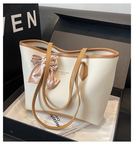 Detailed side view of a white pebble leather tote bag featuring a pink silk scarf bow